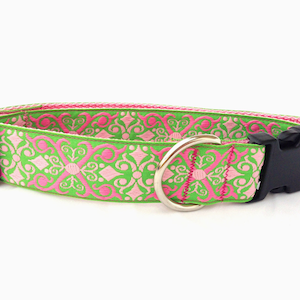 May include: A dog collar with a green and pink floral pattern. The collar has a black plastic buckle and a silver metal D-ring. The collar is made of a woven fabric.