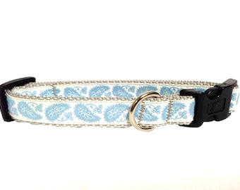 Op de afbeelding: Een witte hondenriem met een blauw paisley-patroon en een zilveren metalen ring. De riem heeft een zwarte plastic gesp.