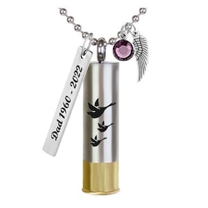 May include: Silver-tone memorial necklace with a cylindrical pendant featuring black flying geese. A rectangular tag reads "Dad 1960 - 2022." Additional charms include a purple gem and a silver wing. The bottom of the pendant is gold-colored.