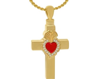 May include: A gold-colored cross pendant with a red heart-shaped center, surrounded by small, clear stones. The pendant hangs from a gold chain. The cross has a detailed design with a textured surface.