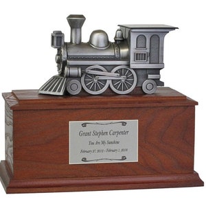 May include: A silver toy train figurine on top of a wooden box. The box has a silver plaque with the inscription "Grant Stephen Carpenter You Are My Sunshine February 27, 2012 - February 1, 2016".