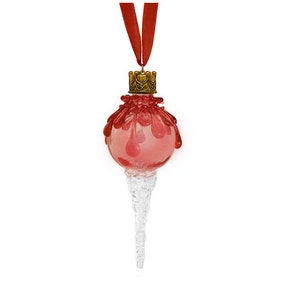 May include: A red glass Christmas ornament with a gold crown on top and a clear icicle-shaped bottom. The ornament is hanging from a red ribbon.