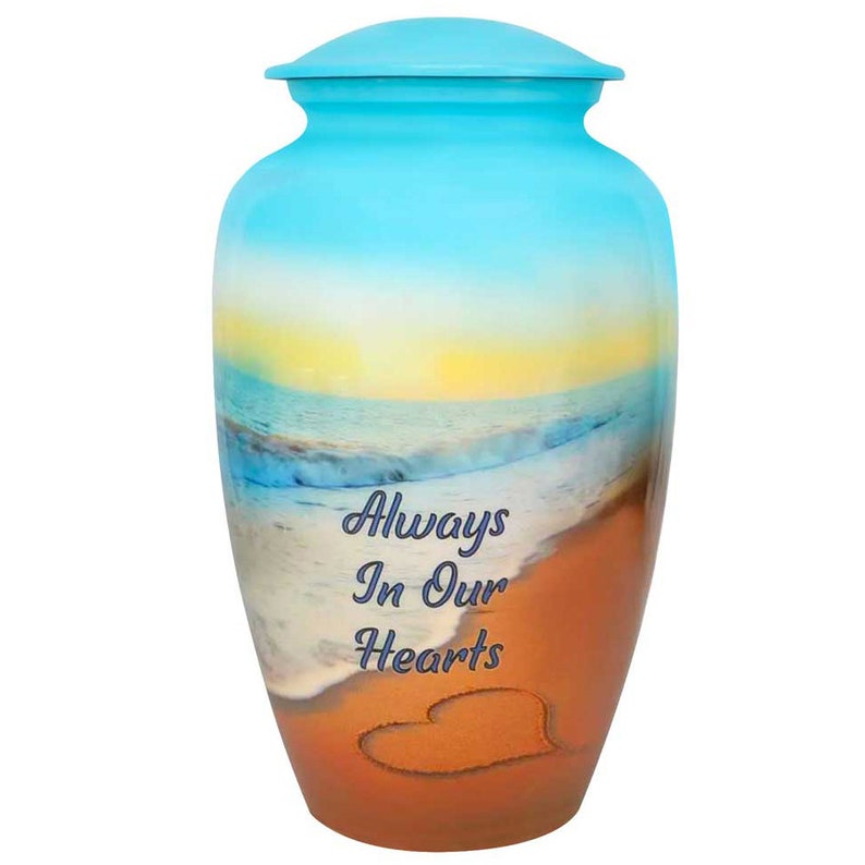 May include: A blue and orange cremation urn with a beach scene and the words "Always In Our Hearts" on the front. A heart is drawn in the sand.