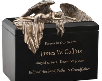 Puede incluir: Una urna funeraria rectangular negra con una figura de ángel en tono bronce sobre la tapa. El frente está grabado con el texto: Forever In Our Hearts, James W. Collins, August 12, 1947 - December 3, 2023, Beloved Husband, Father & Grandfather.