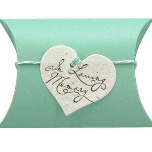 May include: A light green pillow box with a white heart-shaped tag tied with twine. The tag has the text "In Loving Memory" written in cursive.