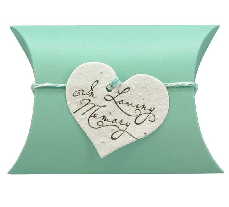 May include: A light green pillow box with a white heart-shaped tag tied with twine. The tag has the text "In Loving Memory" written in cursive.