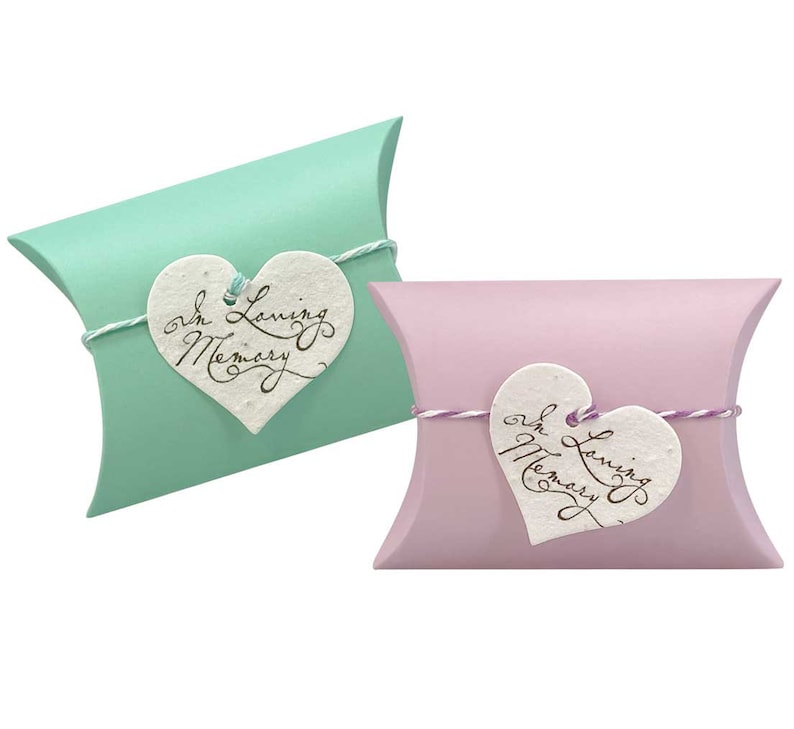 May include: Two pillow boxes, one light green and one light purple, with a white heart-shaped tag attached to each. The tag says "In Loving Memory".