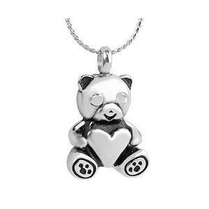 May include: Silver pendant necklace featuring a teddy bear holding a heart. The bear has a detailed face and paw prints on its feet.