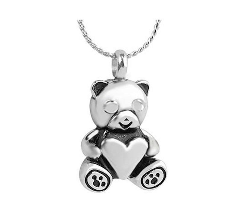 May include: Silver pendant necklace featuring a teddy bear holding a heart. The bear has a detailed face and paw prints on its feet.