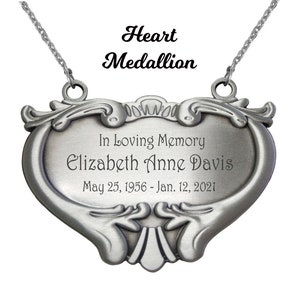 May include: A silver heart-shaped memorial medallion with an inscription that reads "In Loving Memory Elizabeth Anne Davis May 25, 1956 - Jan. 12, 2021".