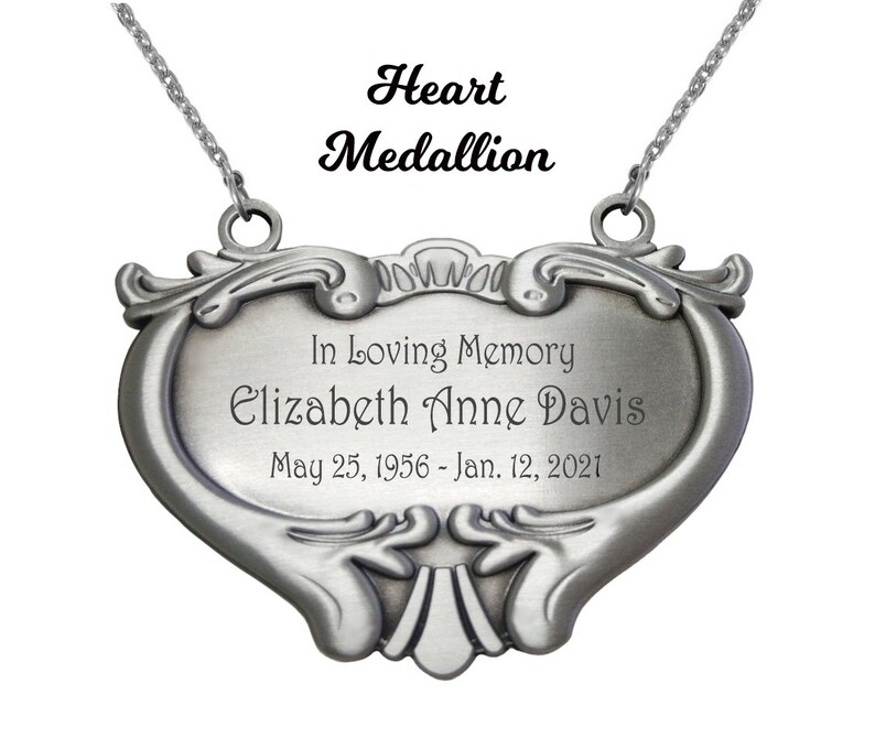 May include: A silver heart-shaped memorial medallion with an inscription that reads "In Loving Memory Elizabeth Anne Davis May 25, 1956 - Jan. 12, 2021".