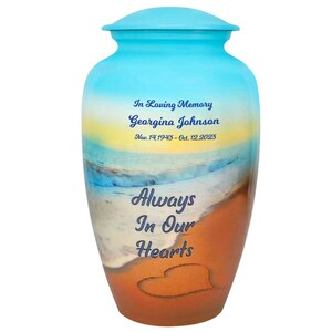 May include: A blue and brown cremation urn with a beach scene and the text "In Loving Memory Georgina Johnson Nov. 14, 1943 - Oct. 12, 2023 Always In Our Hearts".