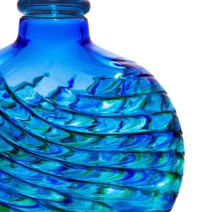 May include: A blue glass bottle with a swirling pattern of blue and green glass. The bottle has a round shape and a wide mouth.
