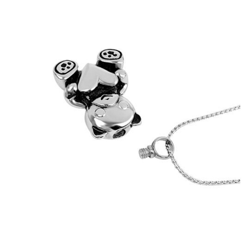 May include: Silver charm necklace featuring a small bear holding a heart. The charm is attached to a silver chain.