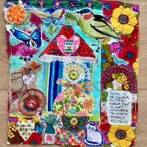 May include: A colorful textile art piece with a patchwork design. It features a house, butterflies, a bird, and floral patterns. The artwork includes the text "THERE IS NO COLOUR IN THIS WORLD THAT IS NOT INTENDED TO MAKE PEOPLE REJOICE."