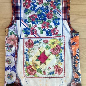 Puede incluir: Un chaleco patchwork hecho con pañuelos vintage y retales de tela. El chaleco presenta diseños florales en rojo, azul y amarillo, con un estampado de cuadros en los hombros y la espalda. Es una prenda única y hecha a mano.