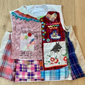 May include: A patchwork vest featuring a variety of fabrics, including plaid, lace, and floral patterns. The vest is adorned with decorative buttons, a heart-shaped patch, and a small boat applique. The color palette includes red, pink, blue, and green.