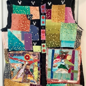 Könnte beinhalten: Eine ärmellose Patchwork-Weste mit schwarzer Basis und bunten Stoffquadraten. Die Weste hat rote Knöpfe, weiße Bullensymbole und verschiedene Muster, darunter Punkte und florale Designs. Sie hat einen Kragen.