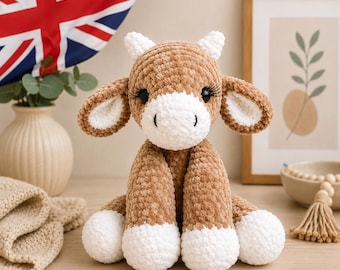 May include: A plush stuffed animal shaped like a cow, crafted from soft brown and white yarn. The toy features long, floppy ears, small white horns, and prominent black eyelashes over dark eyes. The cow has a white muzzle and white hooves.