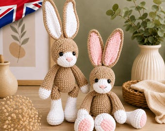 May include: Two crocheted stuffed rabbits made of tan yarn with white accents. The taller rabbit has long white-lined ears, while the shorter rabbit features pink-lined ears and pink foot pads. Both have black safety eyes and white muzzles.