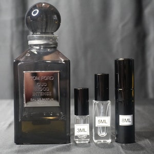 May include: Three bottles of Tom Ford Oud Wood Intense Eau de Parfum. The largest bottle is 50 ml and is dark brown with a silver label. The smaller bottles are 3 ml and 8 ml and are clear glass with black caps.