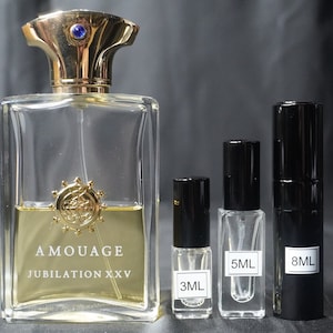 May include: A clear glass bottle of Amouage Jubilation XXV perfume with a gold cap and a blue jewel. Three smaller bottles of perfume are in the foreground, labeled 3ml, 5ml, and 8ml.