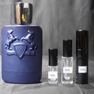 May include: A blue glass bottle of perfume with a silver cap and two horses on the front. The bottle is labeled "Parfums de Marly Paris". There are three smaller bottles of perfume in the background, labeled "3ML", "5ML", and "8ML".