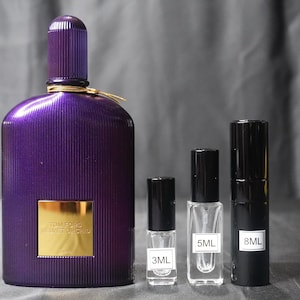 May include: A purple perfume bottle with a gold label and the text "TOM FORD VELVET ORCHID" next to three smaller perfume bottles. The smaller bottles are labeled 3ML, 5ML, and 8ML. The bottles are on a gray surface.