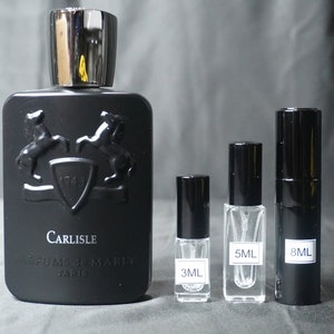 May include: A black bottle of Carlisle perfume by Parfums de Marly with a silver cap. The bottle is next to three smaller bottles of perfume, one 3 ml, one 5 ml, and one 8 ml.