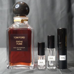 May include: A Tom Ford Ébène Fumée Eau de Parfum bottle with a black cap and a gold label. The bottle is next to three smaller perfume bottles, one clear and two black, with labels indicating 3 ml, 5 ml, and 8 ml.