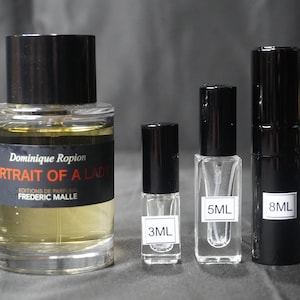 May include: Three glass bottles of perfume with black caps. The largest bottle is labeled "Dominique Ropion Portrait of a Lady Editions de Parfums Frederic Malle". The smaller bottles are labeled "3ML", "5ML", and "8ML".