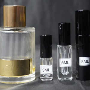 May include: Four glass bottles of perfume in different sizes. The largest bottle is clear with a gold cap and a gold label that says "Tom Ford Private Blend". The other three bottles are smaller and have black caps. The labels on the smaller bottles say "3ML", "5ML", and "8ML".