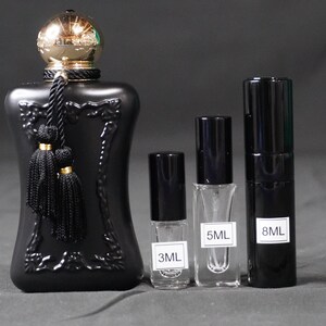 May include: Four black glass perfume bottles with gold accents. The largest bottle has a black tassel and a gold cap. The bottles are labeled 3ML, 5ML, and 8ML.