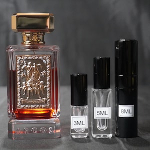 May include: Four perfume bottles, one large and three small. The large bottle is clear glass with a gold top and a gold label with a design of three figures on horseback. The small bottles are clear glass with black tops and labels that say "3ML", "5ML", and "8ML".