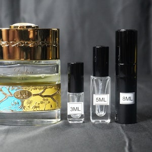May include: A clear glass bottle with a gold lid and a blue and yellow label. The bottle is surrounded by three smaller bottles, one with a clear glass body and a black lid, one with a clear glass body and a gold lid, and one with a black glass body and a black lid. The bottles are labeled with the volume in milliliters: 3ML, 5ML, and 8ML.