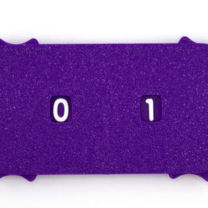 May include: A purple, textured counter with a unique, starburst-like edge. The counter displays the numbers "0" and "1" in white, centered within rectangular cutouts. The object is likely used for counting or tracking.