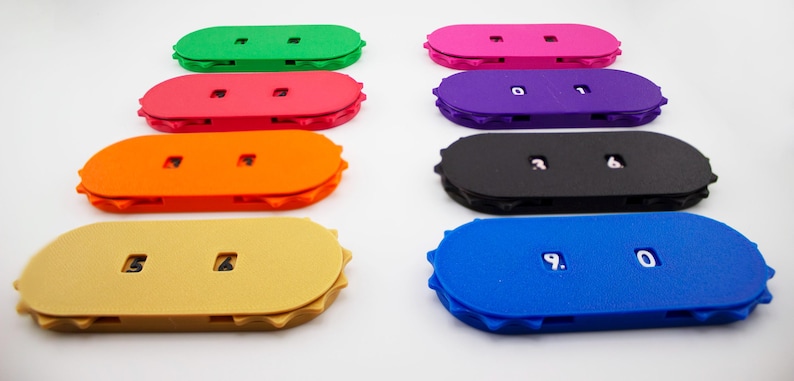 May include: A collection of colorful, oval-shaped bottle cap openers in various colors, including green, pink, orange, and blue. Some openers have numbers printed on them.