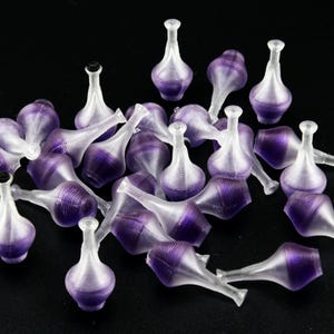 May include: A collection of small, clear, decorative glass bottles with a purple liquid inside. Each bottle has a long, thin neck and a small, black stopper. The bottles are scattered on a black surface.