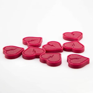 Puede incluir: Una colección de nueve objetos en forma de corazón de color rojo intenso, cada uno con un diseño de grieta. Los objetos están dispersos sobre una superficie blanca, creando un contraste llamativo. Los corazones parecen estar hechos de un material sólido.
