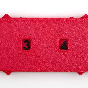 May include: A textured, bright red rectangular object with rounded ends and a sunburst-like edge. The number 3 is in a square on the left, and the number 4 is in a square on the right. The object is on a white background.