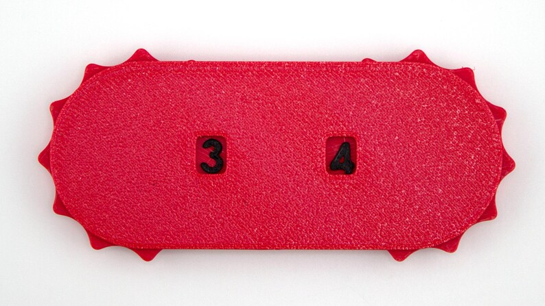May include: A textured, bright red rectangular object with rounded ends and a sunburst-like edge. The number 3 is in a square on the left, and the number 4 is in a square on the right. The object is on a white background.