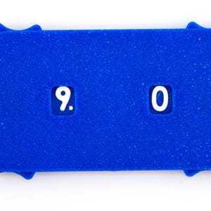 May include: A bright blue, rectangular counter with rounded ends and a sunburst design. The counter displays the numbers "9. 0" in white. The item is set against a white background.