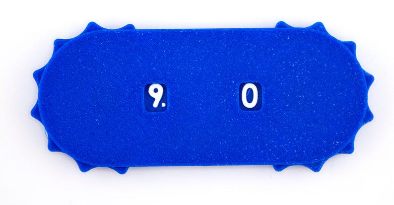 May include: A bright blue, rectangular counter with rounded ends and a sunburst design. The counter displays the numbers "9. 0" in white. The item is set against a white background.