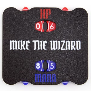 Könnte beinhalten: Ein schwarzer, rechteckiger Spielzähler mit abgerundeten Ecken, rotem HP-Schriftzug über zwei roten Drehscheiben mit den Zahlen 0 und 6. Mittig steht MIKE THE WIZARD in Weiß, darunter blaue Drehscheiben mit 8 und 5 sowie der blaue Schriftzug MANN.