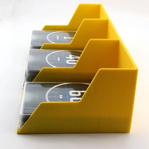 May include: A bright yellow plastic card organiser featuring three distinct tiered slots designed to hold stacks of playing cards. Each slot contains a deck of cards with visible black and white circular graphics and the numbers 40 and 60 printed.