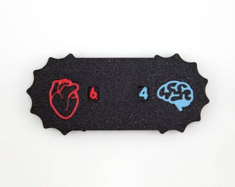 Puede incluir: Una insignia rectangular negra con superficie texturizada y bordes festoneados. Presenta un icono de corazón rojo bordado junto al número 6, y un icono de cerebro azul claro bordado junto al número 4, dispuestos en una fila horizontal.