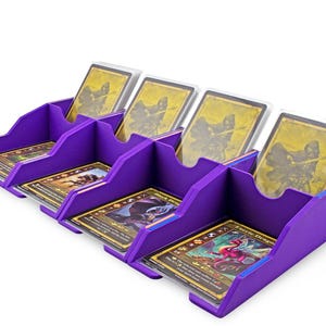 May include: A purple card organizer with four compartments, each holding trading cards. The cards are in protective sleeves. The organizer is designed to keep cards organized and accessible.