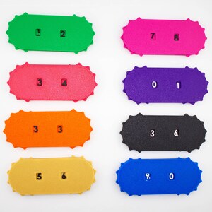 May include: Eight colorful, rectangular number cards with scalloped edges. Each card displays a different number combination in white. Colors include green, pink, red, purple, orange, black, yellow, and blue. The numbers are clearly printed.