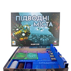 May include: Board game box titled "ПІДВОДНІ МІСТА" in blue and white. The box is open, revealing game components such as cards and tokens. The game's theme is an underwater city. The box is open, revealing the game's contents.