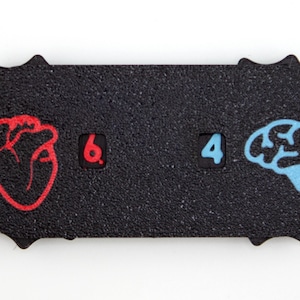 May include: A black, textured, rectangular object with a unique, starburst-like edge. It features a red heart graphic, the number 6, the number 4, and a blue brain graphic. The design is simple and graphic.